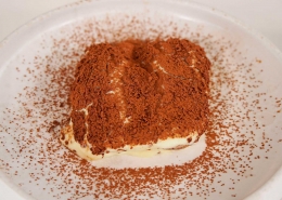 Et stykke tiramisu serveret med drysset kakaopulver