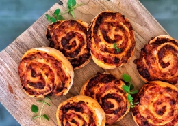 Syv bagte pizzasnegle på et skærebræt med frisk oregano som pynt